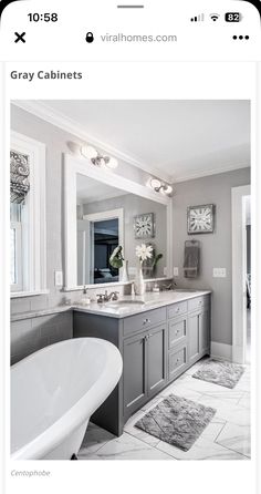 a bathroom with gray cabinets and white bathtub next to a large mirror on the wall