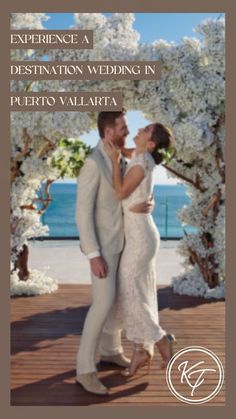 a man and woman are kissing in front of an archway with white flowers on it