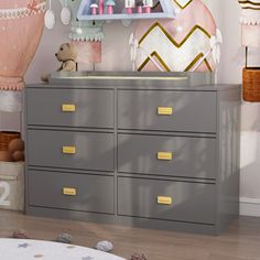 a baby's room with pink and gold decorations on the wall, gray dresser