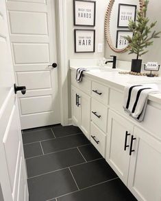 a white bathroom with black tile flooring and pictures on the wall above the sink