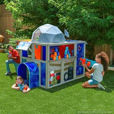 two children playing in a play house with an adult and one child sitting on the grass