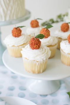 cupcakes with white frosting and orange sprinkles are on a cake plate