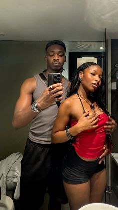 a man and woman standing in front of a bathroom mirror looking at their cell phones