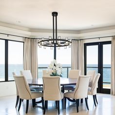 a dining room table with chairs and chandelier in front of large windows overlooking the ocean