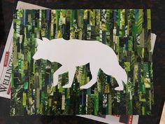 a paper cut out of a white wolf on top of green and black strips of newspaper