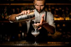 the bartender is making a drink at the bar with his hand on the shaker