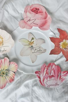 four plates with flowers on them sitting on a white cloth covered tablecloth, one has the names of three different types of flowers