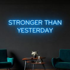 two chairs and a table in front of a neon sign that says, stronger than yesterday