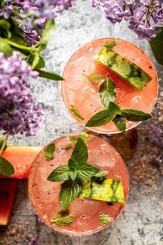 two glasses filled with watermelon and cucumber garnish next to slices of watermelon