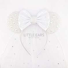 a white dress with pearls and a big bow on the headband that says little ears boutique