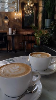 two cups of cappuccino sit on a table in a restaurant with chandeliers