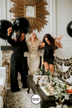 three women standing in front of a table with black balloons