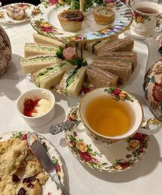 a table topped with plates and cups filled with tea next to sandwiches, muffins and scones