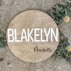 a wooden sign with the word blakelyn on it in front of some dandelions