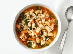 a white bowl filled with pasta and spinach soup on top of a table next to a spoon