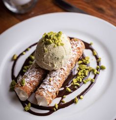 two desserts on a white plate with chocolate sauce and pistachio