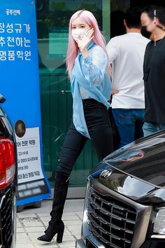 a woman with pink hair and black pants walking down the street in front of a car