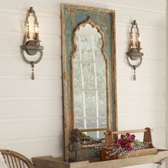 an old mirror is hanging on the wall next to a table with flowers in it