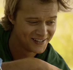 a young man smiles as he looks at his cell phone while wearing a green shirt