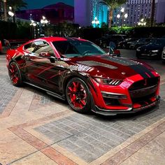 a red and black car parked in front of a tall building at night with its lights on