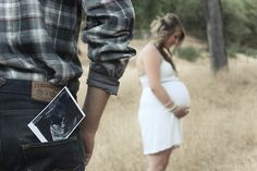 a pregnant woman standing next to a man in a field with trees and grass behind her