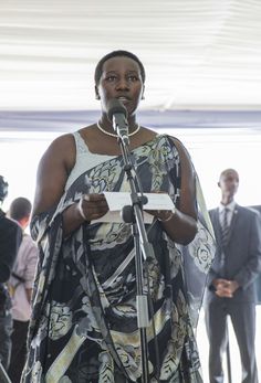 a woman standing in front of a microphone holding a piece of paper and looking at the camera