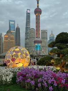 the city skyline is lit up at night with flowers and trees in front of it