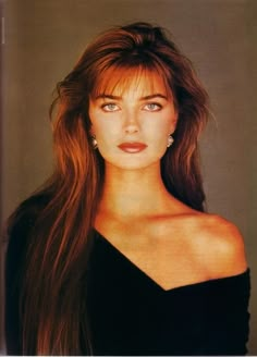 a woman with long brown hair wearing a black dress and diamond earrings, looking at the camera