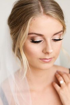 a woman wearing a veil and makeup looks down at her wedding ring on her finger