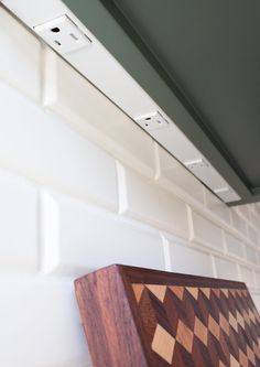 a wooden cutting board sitting on the side of a white brick wall next to a stove