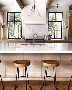 three stools sit in front of an island with marble countertops and wooden flooring