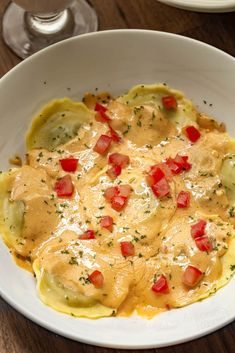 a white bowl filled with ravioli covered in cheese sauce and topped with red peppers