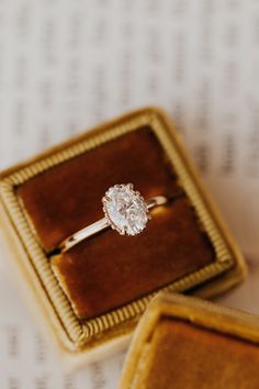 an engagement ring sitting in a box on top of a piece of paper next to it