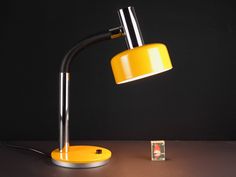 a yellow desk lamp sitting on top of a table next to a small square object