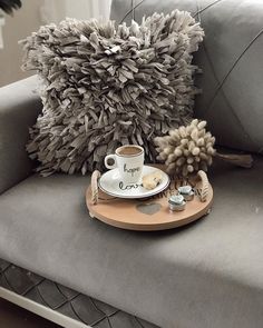 a coffee cup and saucer sitting on top of a gray couch next to a pillow