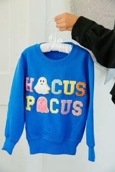 Get your little ones ready for some magic this season with our MINI KIDS HOCUS POCUS BLUE PULLOVER. This blue pullover features rainbow mini glam Hocus Pocus letters and a white and pink glam ghost patch, adding a touch of whimsy to any outfit. Perfect for the young spellcaster in your life! All orders are currently shipping within 14 business days. To receive item quicker, expedited shipping is available at checkout. **ALL HALLOWEEN ORDERS MUST BE PLACED WITH EXPEDITED SHIPPING TO GUARANTEE DEL Usa Party, Mini Sales, Pink Glam, Thanksgiving Sale, Valentines Sale, Cheer Dance, Baseball Trucker Hat, Blue Pullover, Bride Accessories