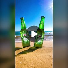 two bottles of beer sitting on top of a sandy beach