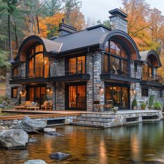 a large house sitting on top of a lush green hillside next to a river in front of a forest