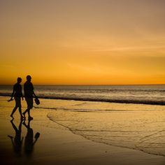 two people walking on the beach at sunset