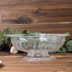 a clear glass bowl sitting on top of a wooden table next to flowers and leaves