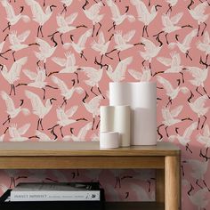 a pink wall with white birds on it and a book shelf in the foreground