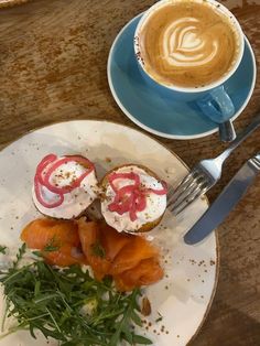 a white plate topped with food on top of a wooden table next to a cup of coffee