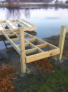 a wooden dock sitting on top of a grass covered field next to a body of water