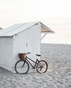 a bike parked next to a white building on top of a sandy beach with the ocean in the background