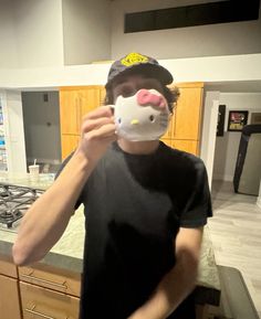 a man with a hello kitty mask covering his face while standing in front of a kitchen counter