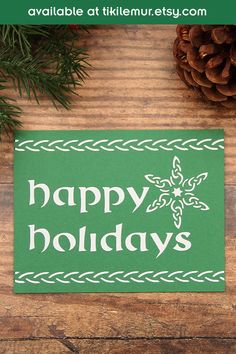 a green sign that says happy holidays on it next to pine cones and evergreen needles