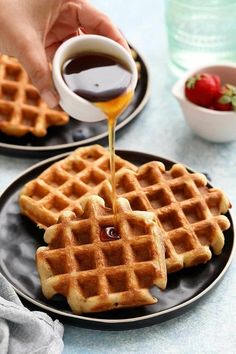 someone is pouring syrup onto some waffles on a black plate with strawberries