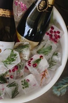 two bottles of champagne and some ice cubes on a table with christmas decorations around it