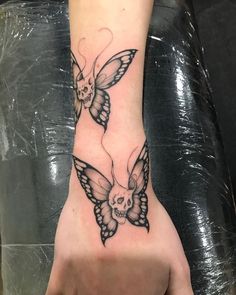 a person's hand with a butterfly and skull tattoo on the left side of their wrist