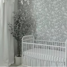 a white crib in front of a wall with flowers on it and a potted plant next to the crib